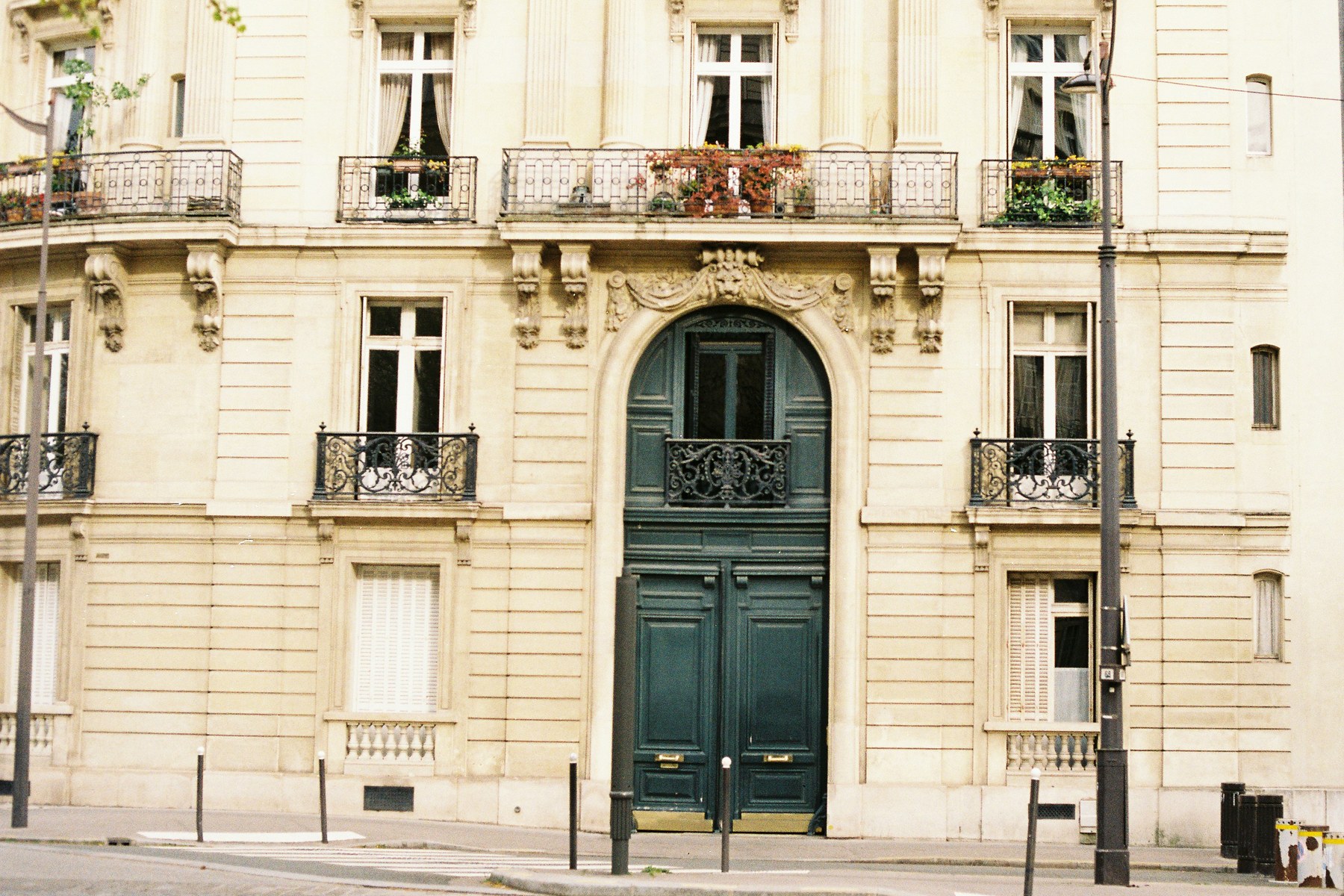 Porte cochère en bois vert sombre encadrée de pierre sculptée, façade haussmannienne, balcons en fer forgé garnis de fleurs.