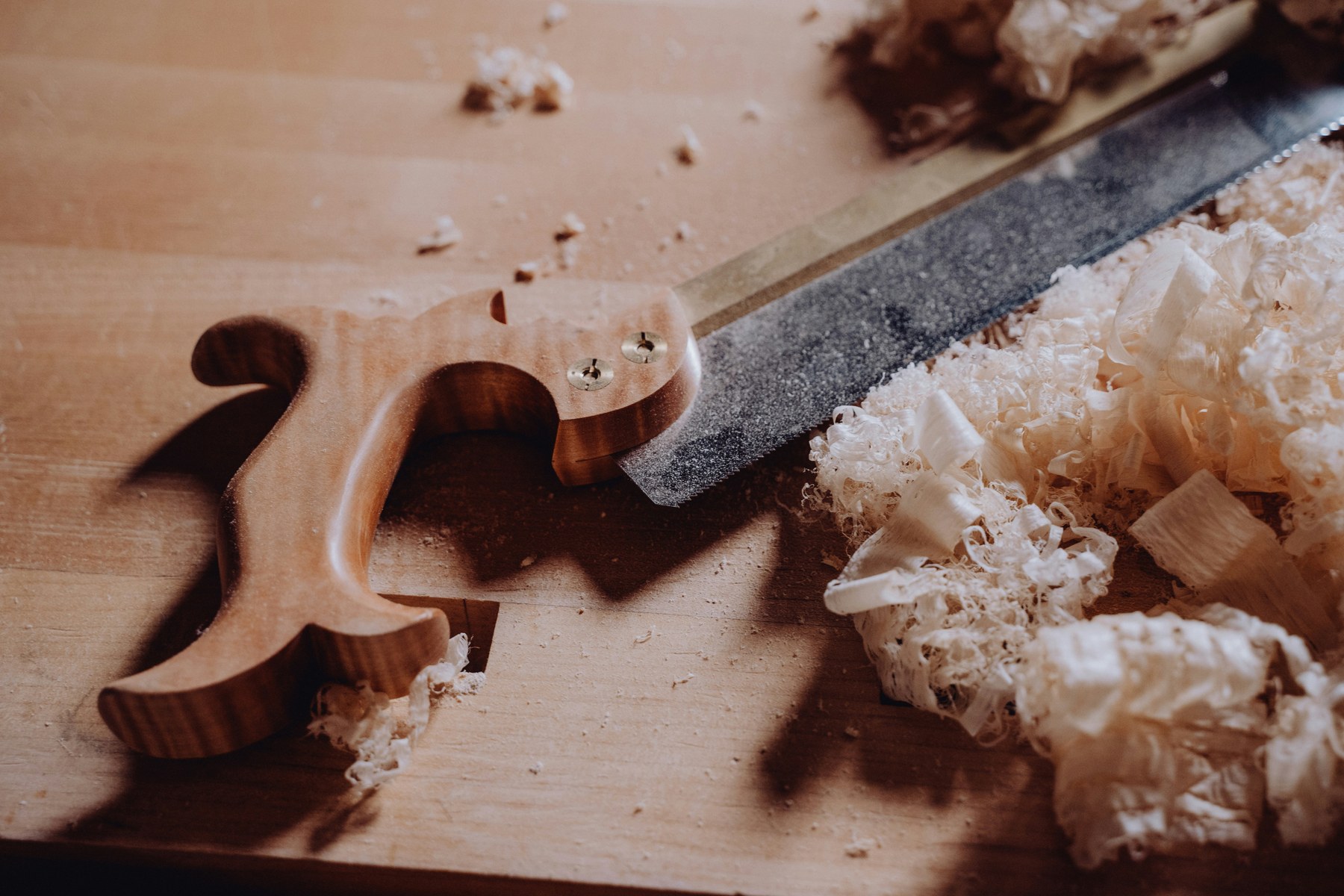Scie égoïne posée sur un plan de travail clair, copeaux fins répandus à droite — outils du métier de l'artisan.