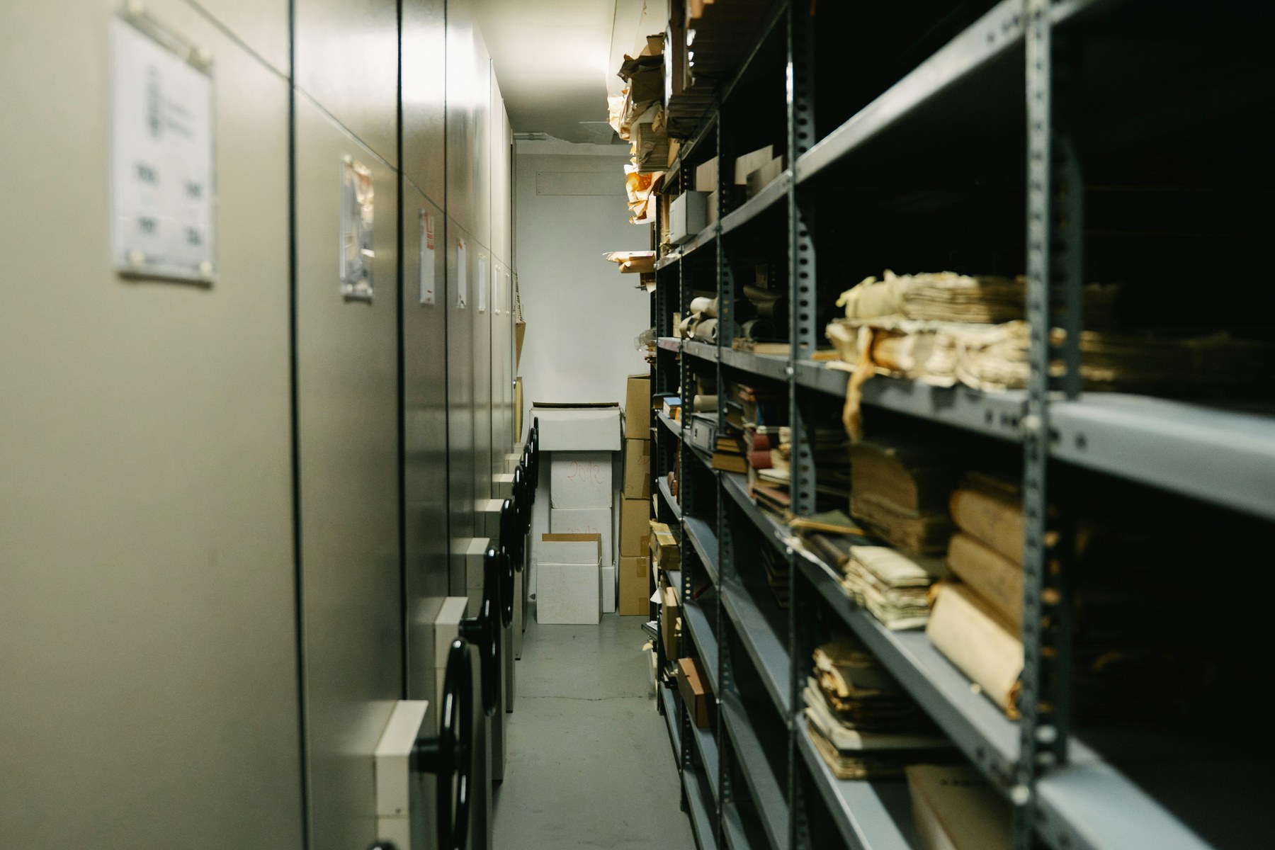 Couloir d'archives sur rayonnages mobiles : dossiers et registres organisés sur plusieurs étages.