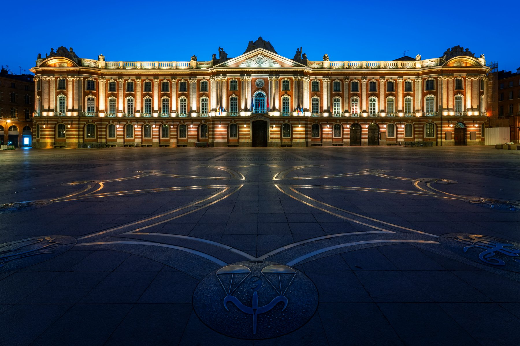 Façade néo-classique du Capitole de Toulouse à l'heure bleue, place déserte en avant-plan.