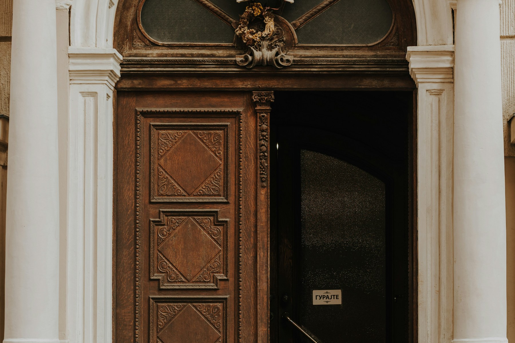 Porte cochère sculptée entrouverte sur l'entrée d'un immeuble, encadrement en pierre arqué, vue depuis la rue.