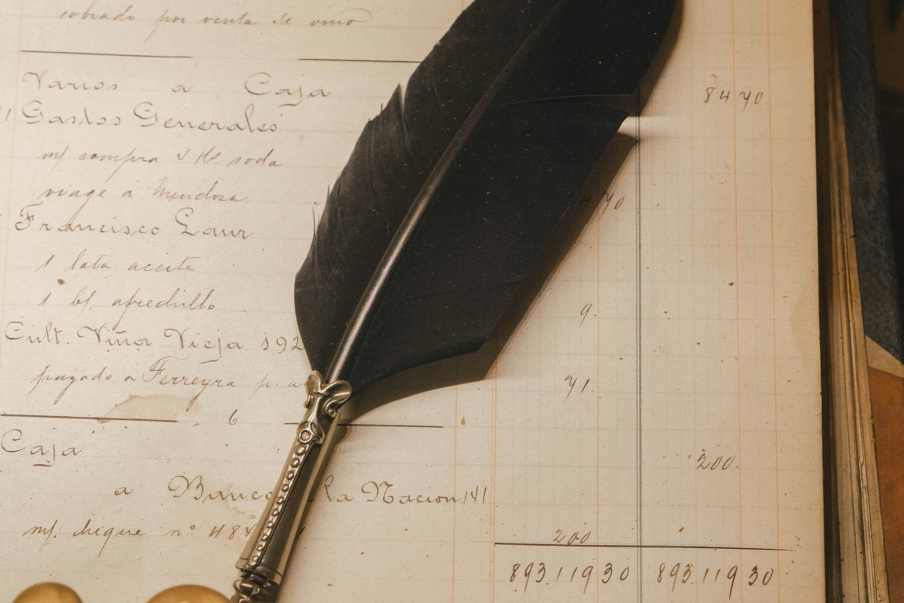 Registre de paie ancien à colonnes manuscrites, plume noire posée sur les inscriptions, encriers en arrière-plan.
